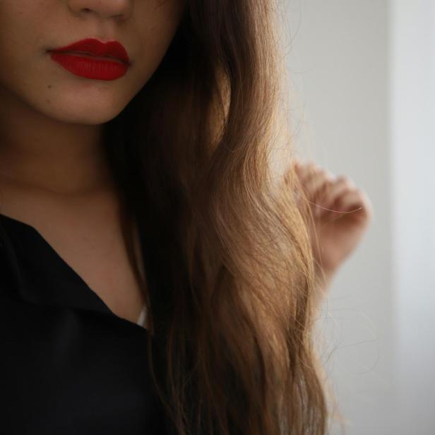 Frau mit langen, gepflegten Haaren und rotem Lippenstift vor hellem Hintergrund.