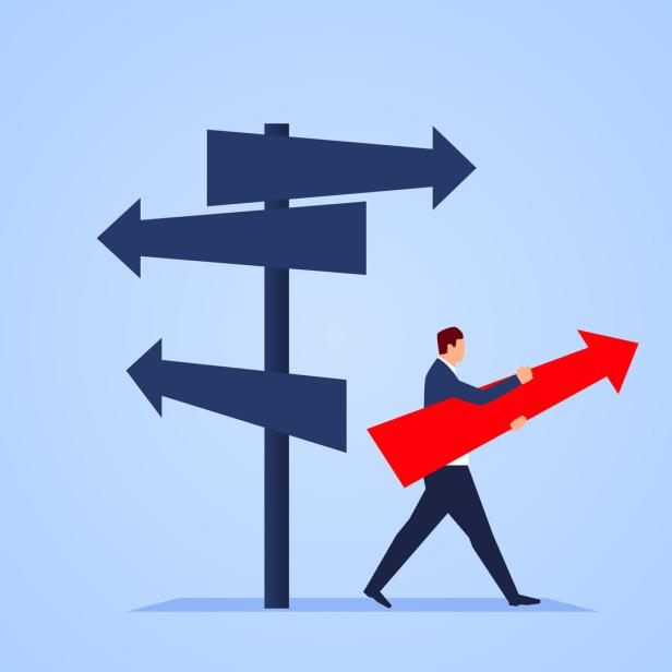 Ein Mann im Anzug trägt einen großen roten Pfeil nach rechts an mehreren Wegweisern mit unterschiedlichen Richtungen vorbei.