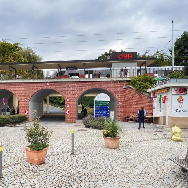 Ein ÖBB-Zug fährt über eine rote Backsteinbrücke mit Durchgängen, neben einem Platz mit einem Eisstand namens "Bella Rosa".