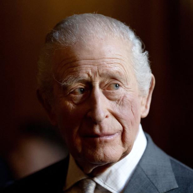 König Charles im Anzug blickt nach rechts, der Hintergrund ist dunkel und unscharf.