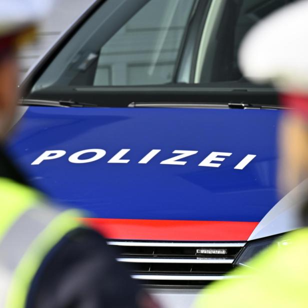 Zwei Polizisten stehen vor einem Polizeiauto mit blau-roter Motorhaube und dem Schriftzug „Polizei“.