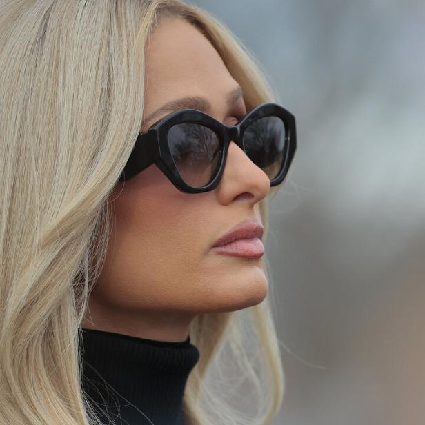 Paris Hilton mit Sonnenbrille und schwarzem Rollkragenpullover blickt zur Seite.