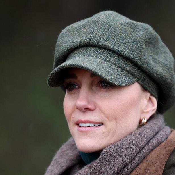 Prinzessin Kate mit grünem Schirmmütze und braunem Schal blickt lächelnd nach vorn.