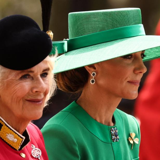 Camilla und Kate, beide mit Hut, schauen in die gleiche Richtung und lächeln.