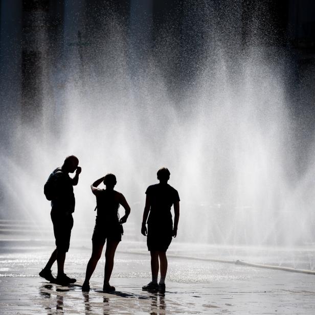 Drei Personen stehen vor einem großen Wasserstrahl, der aus mehreren Düsen aufsteigt.