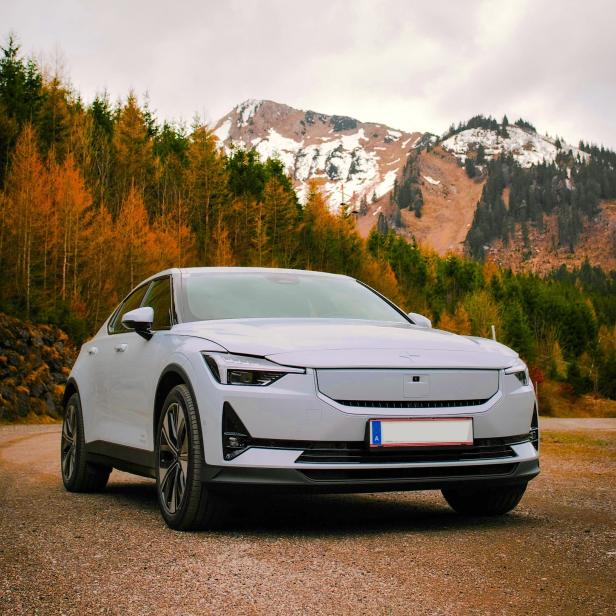 Ein weißes E-Auto steht auf einer Straße, dahinter ist herbstliche Landschaft zu sehen