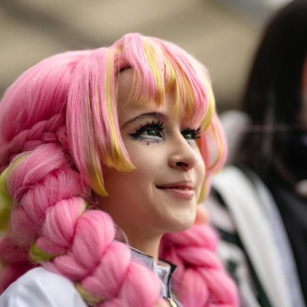 Eine junge Frau mit rosa-gelber Perücke und auffälligem Augen-Make-up lächelt.