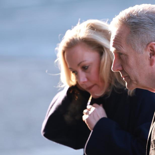 Bettina Wulff mit ernstem Gesichtsausdruck steht im Freien bei kühlem Wetter.