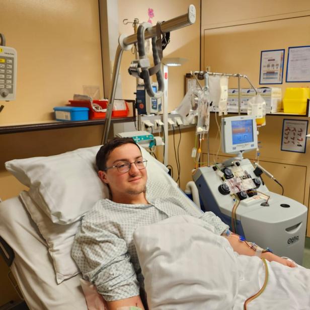 Ein junger Mann liegt im Krankenhausbett und ist an medizinische Geräte zur Blutbehandlung angeschlossen.