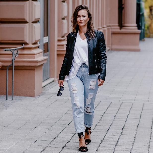 Eine Frau in Jeans und Lederjacke läuft eine Straße lang 
