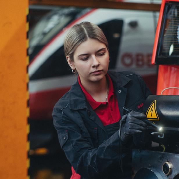 Eine Frau in einer Werkstatt schraubt an einer Zuggarnitur.