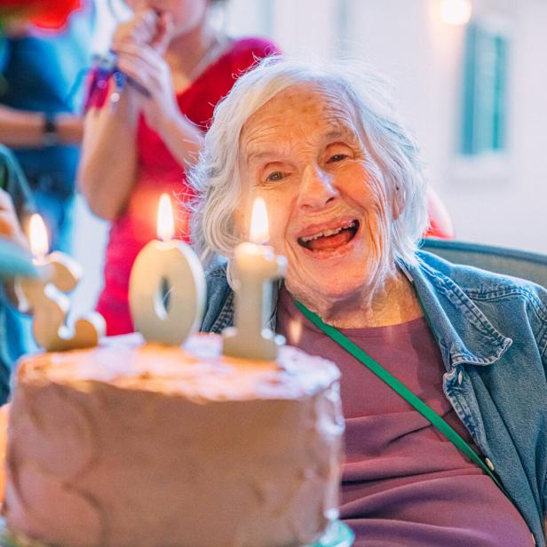 Smiling, Excited Elderly Woman Looks to the "103" Birthday Candles on a Cake
