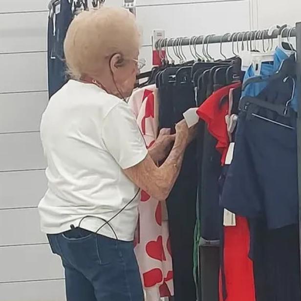92-jährige Frau mit weißem T-Shirt steht vor einer Kleiderstange mit Kleidung
