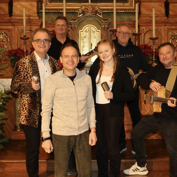 Eine Musikgruppe mit Gitarren und Mikrofonen posiert vor einem verzierten Altar und Weihnachtsbäumen.