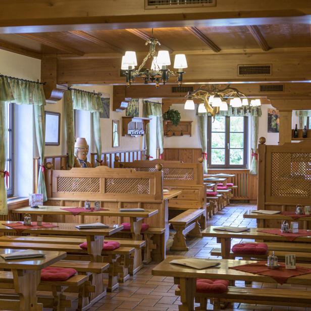 Gemütlicher Gastraum mit Holzmöbeln, roten Sitzpolstern und dekorativen Lampen.