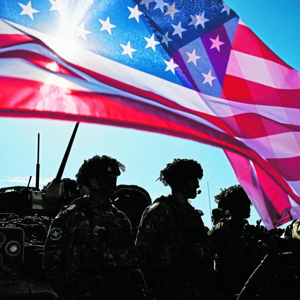 Soldaten stehen vor einem Panzer unter einer wehenden US-Flagge.