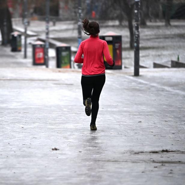 Eine Person joggt auf einem vereisten Gehweg entlang eines Geländers in einer winterlichen Umgebung.