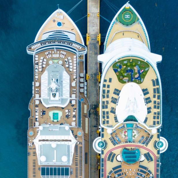 Zwei große Kreuzfahrtschiffe liegen nebeneinander an einem Pier im blauen Meer.