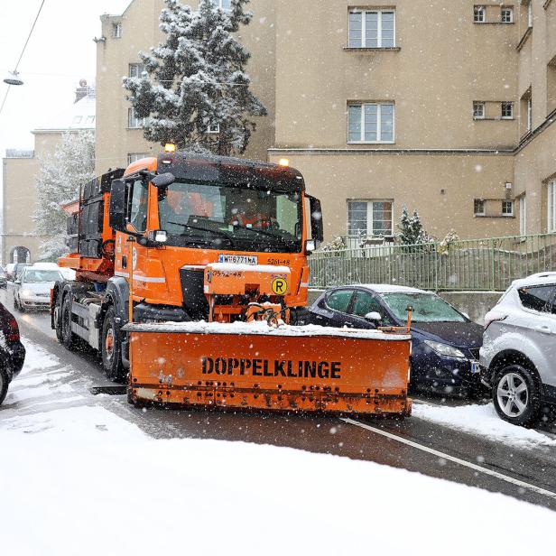 Ein orangenes Räumfahrzeug der MA 48 fährt durch eine schneebedeckte Gasse.