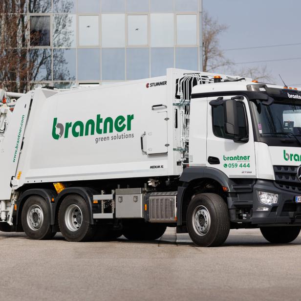 Weißer Müllwagen der Marke Brantner vor einem Gebäude.
