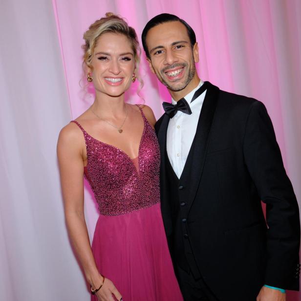 Eine Frau im glitzernden pinken Abendkleid steht lächelnd neben einem Mann im schwarzen Smoking mit Fliege.