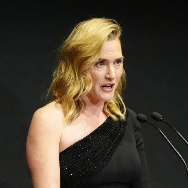 Kate Winslet hält eine Rede an einem Rednerpult mit Mikrofonen.