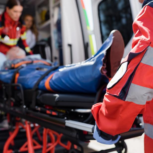 Selective focus of paramedic in uniform carrying stretcher with patient in ambulance ca outdoors