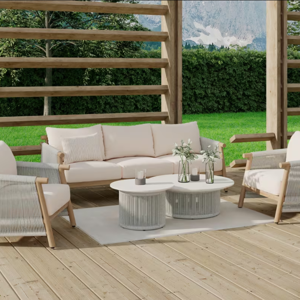 Helle Outdoor-Sitzgruppe mit Sofa, zwei Sesseln und zwei runden Tischen auf einer Holzterrasse, umgeben von viel Grün.