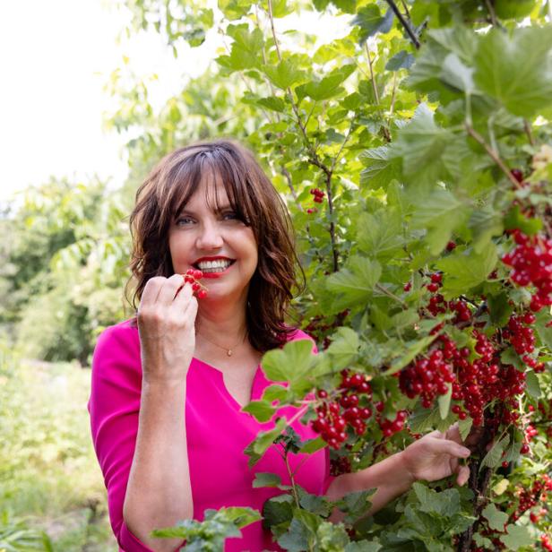 Eine Frau im pinkfarbenen Kleid isst rote Johannisbeeren vom Strauch.