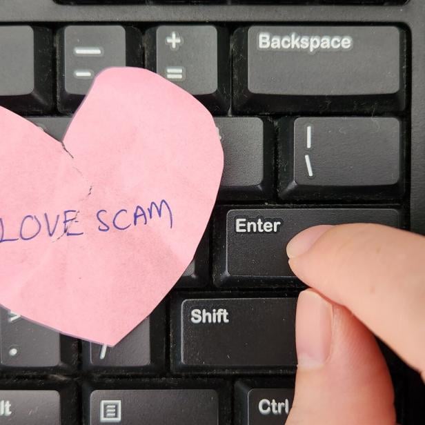 Love Scam awareness concept. A person typing on keyboard sending message to scammer and a crumpled heart with the text Love Scam written on placed on the keyboard