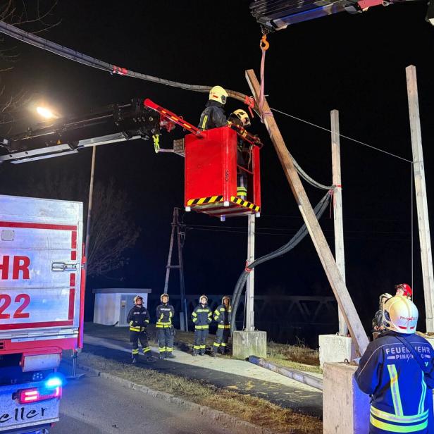 Feuerwehrleute arbeiten nachts mit einem Kran an einer beschädigten Stromleitung und sichern den Bereich.