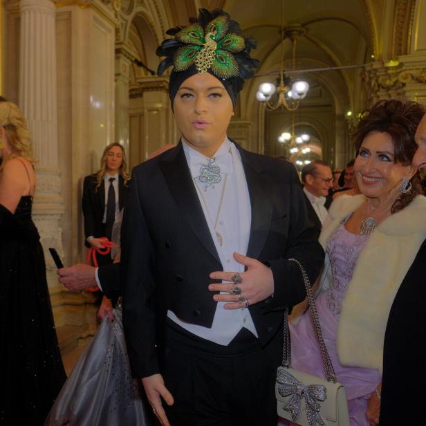 Ein Mann mit Turban und Pfauenfedern posiert mit elegant gekleideten Personen.