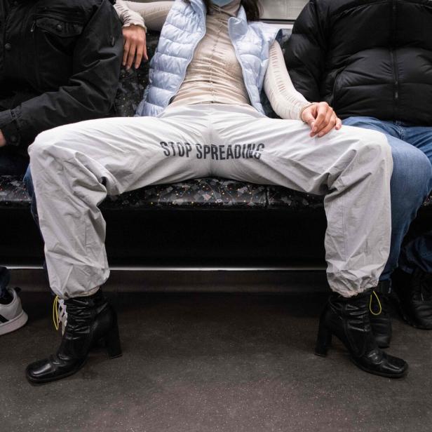 Frau sitzt mit breiten Beinen zwischen zwei Männern in einem öffentlichen Verkehrsmittel