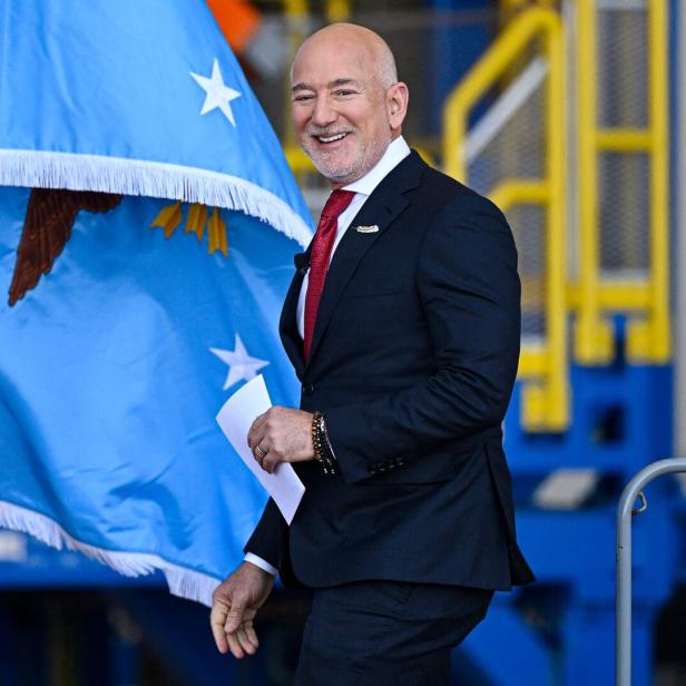 Ein Mann im Anzug und mit roter Krawatte vor einer blauen Flagge
