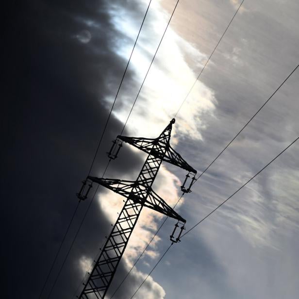 Ein Strommast steht vor einem bewölkten Himmel, durch den die Sonne scheint.