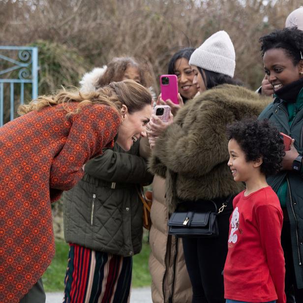 Kate beugt sich lächelnd einem Kind zu, während Umstehende Fotos machen.