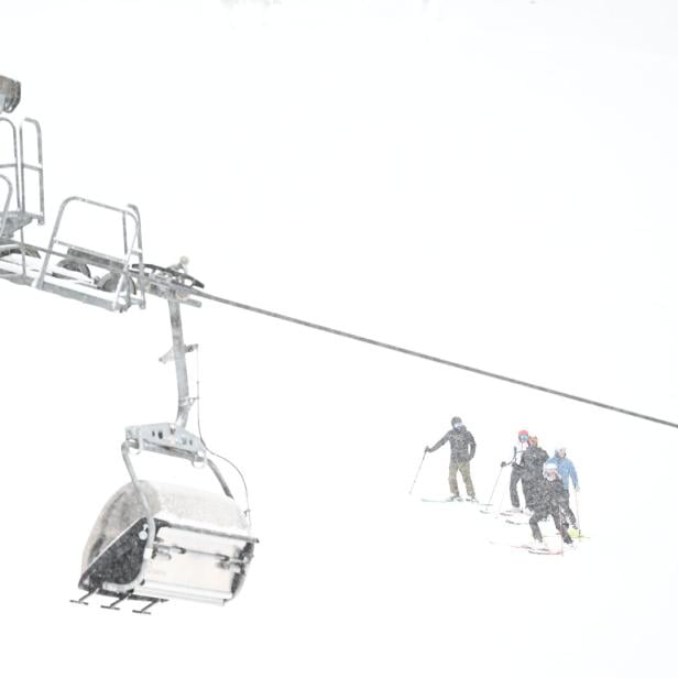 Eine Gondelbahn schwebt über Skifahrer in dichtem Schneefall.