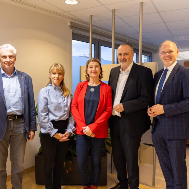 Fünf Personen stehen nebeneinander in einem modernen, hellen Raum und lächeln in die Kamera.