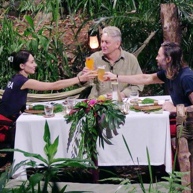 Am festlich gedeckten Tisch mitten im Dschungel stoßen Samira Yavuz, Hubert Fella und Gil Ofarim auf die Dschungelzeit an.