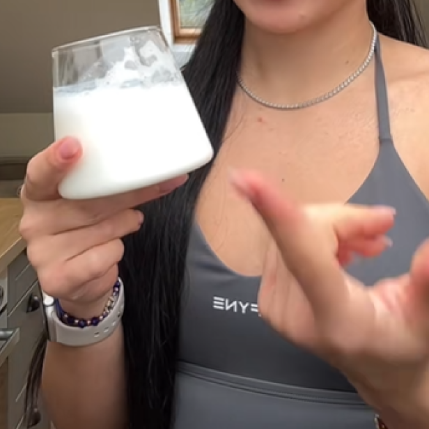Eine junge Frau hält ein Glas mit einem weißen, schaumigen Getränk, das dem aktuellen TikTok-Trend mit Topfen und Energy Drink entspricht.
