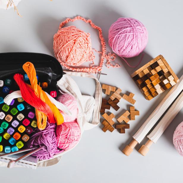 Analog bag of yarn, markers, a notebook, knitting needles, and puzzles top view web banner