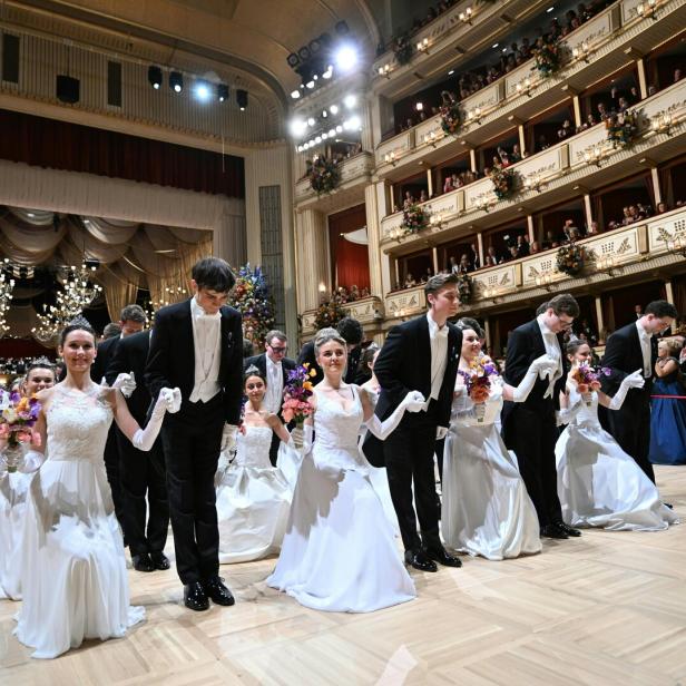 Mehrere Paare in festlicher Kleidung knien auf einem Ballsaal, umgeben von elegantem Publikum auf Balkonen.