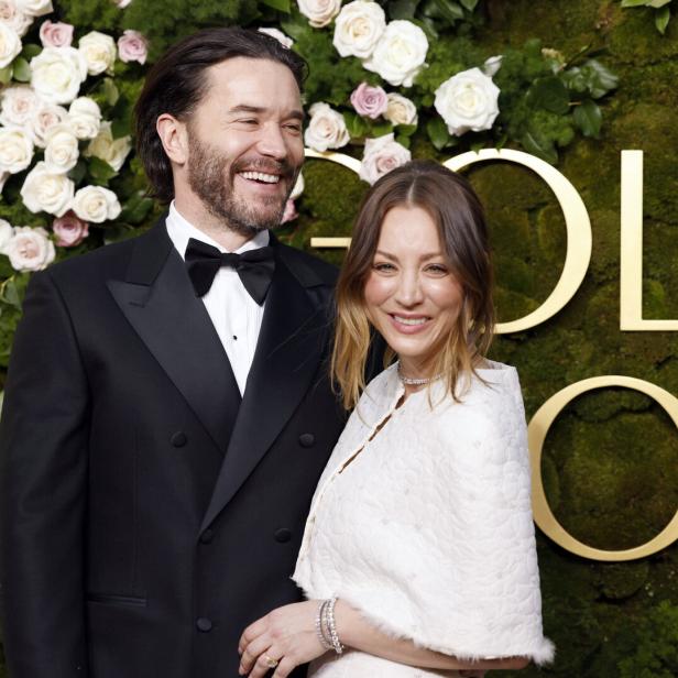 Kaley Cuoco und Tom Pelphrey, er im Smoking, sie in Weiß, posiert vor einem floralen Hintergrund.