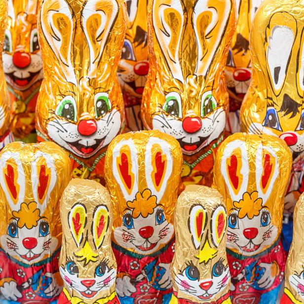 Viele goldene Schokoladenhasen mit aufgemalten Gesichtern stehen dicht nebeneinander.