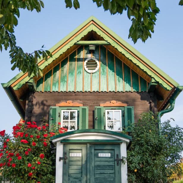 Ein kleines, dunkles Holzhaus mit grünen Akzenten und roten Rosenbüschen davor.