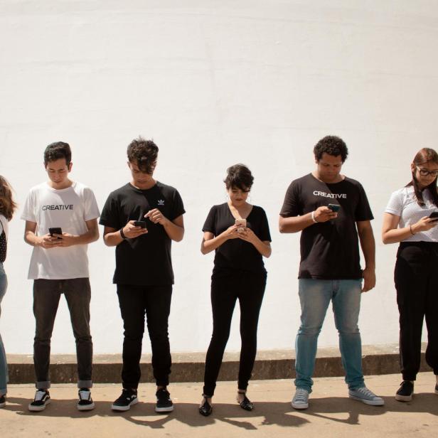 Sechs junge Erwachsene stehen nebeneinander und schauen auf ihre Smartphones.