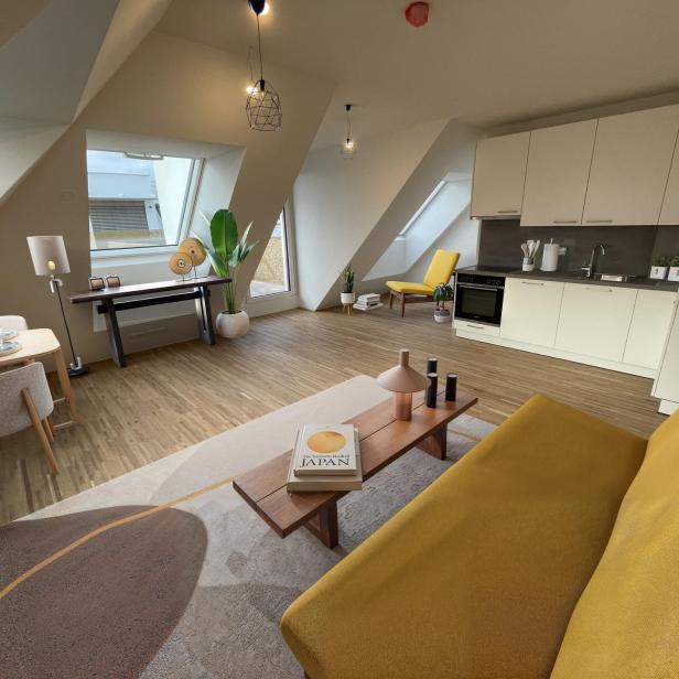 Helles, modern eingerichtetes Wohnzimmer mit gelbem Sofa, Essbereich, offener Küche und großen Fenstern unter Dachschrägen.