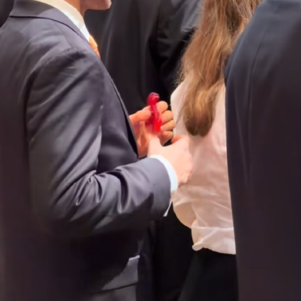 Ein junger Mann im Anzug dreht auf dem Opernball einen roten Fidget Spinner in der Hand.