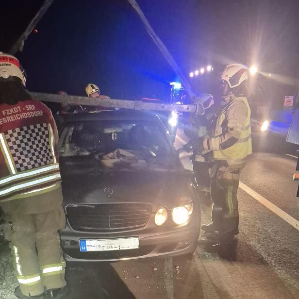 Feuerwehrleute bergen nachts ein beschädigtes Auto auf der Autobahn mit einem Kran.