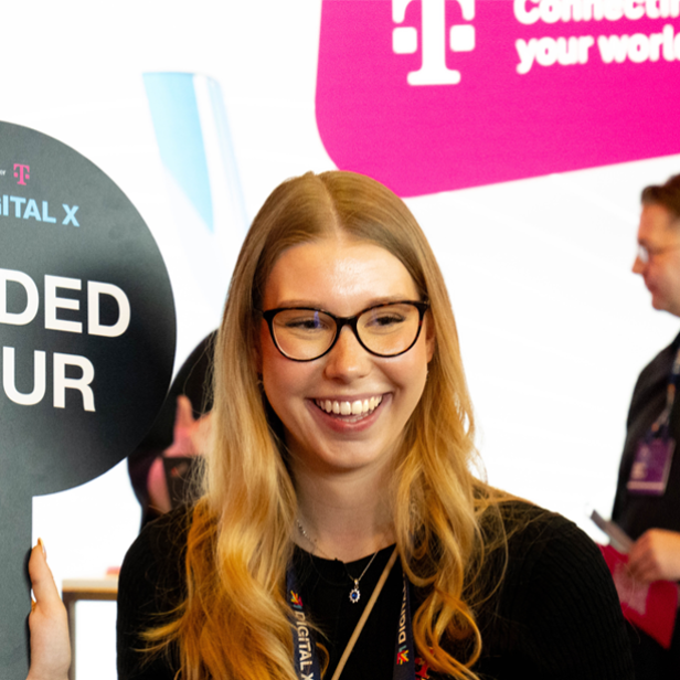 Junge Frau mit "Guided Tour"-Schild auf der DIGITAL X, im Hintergrund Messebesucher.